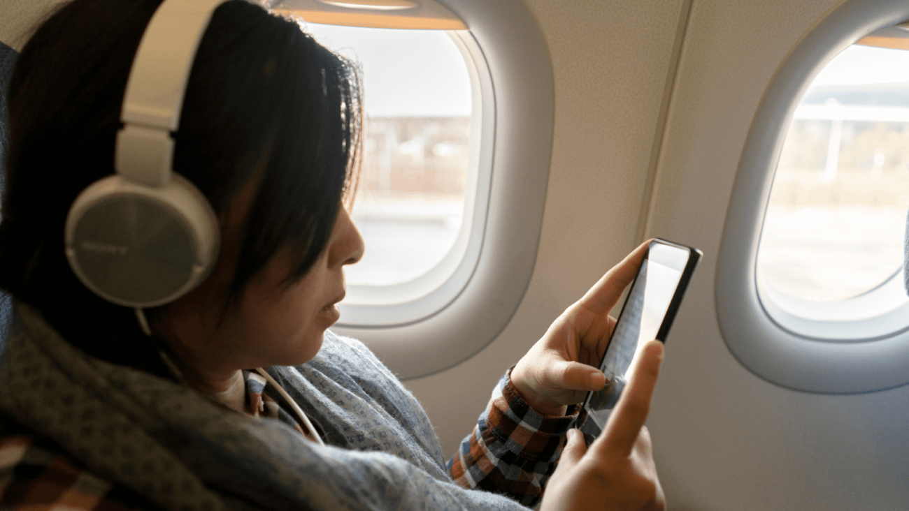 אישה במטוס משחקת בטלפון באמצעות חבילת גלישה